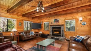 A wooden cabin interior with a fireplace, leather sofas, a television, and a stone fireplace surround. - Black Diamond | Family & Pet-Friendly Cabin Near Huntington Lake (Big Creek)