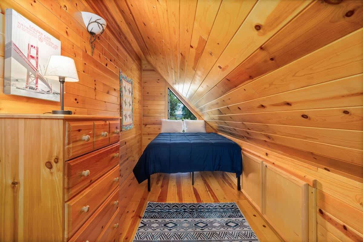 Un dormitorio de cabaña de madera con cama, cómoda, lámpara y un cartel en la pared.