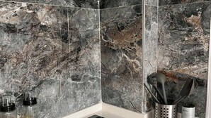 Una cucina con piano cottura nero, cappa in acciaio inossidabile e schienale in marmo.