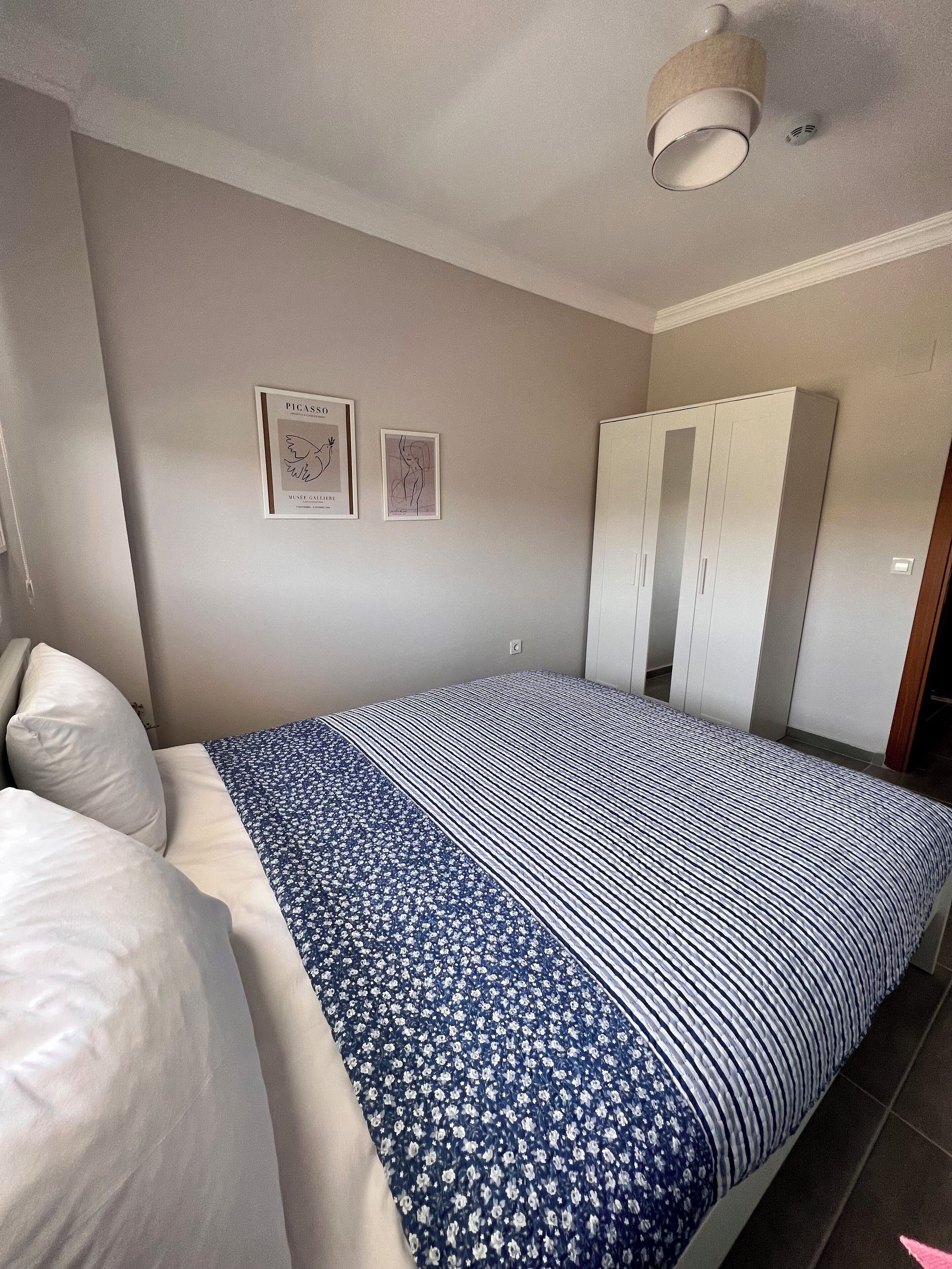 A bedroom with a bed, a wardrobe, and two framed artworks on the wall.