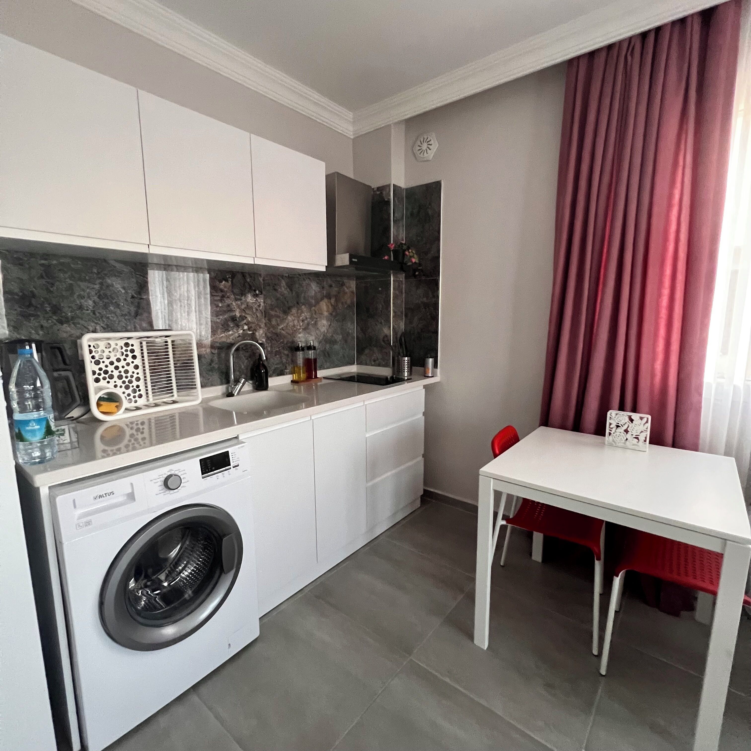 Una cocina compacta con lavadora, un lavamanos y una zona de comedor con mesa y sillas.