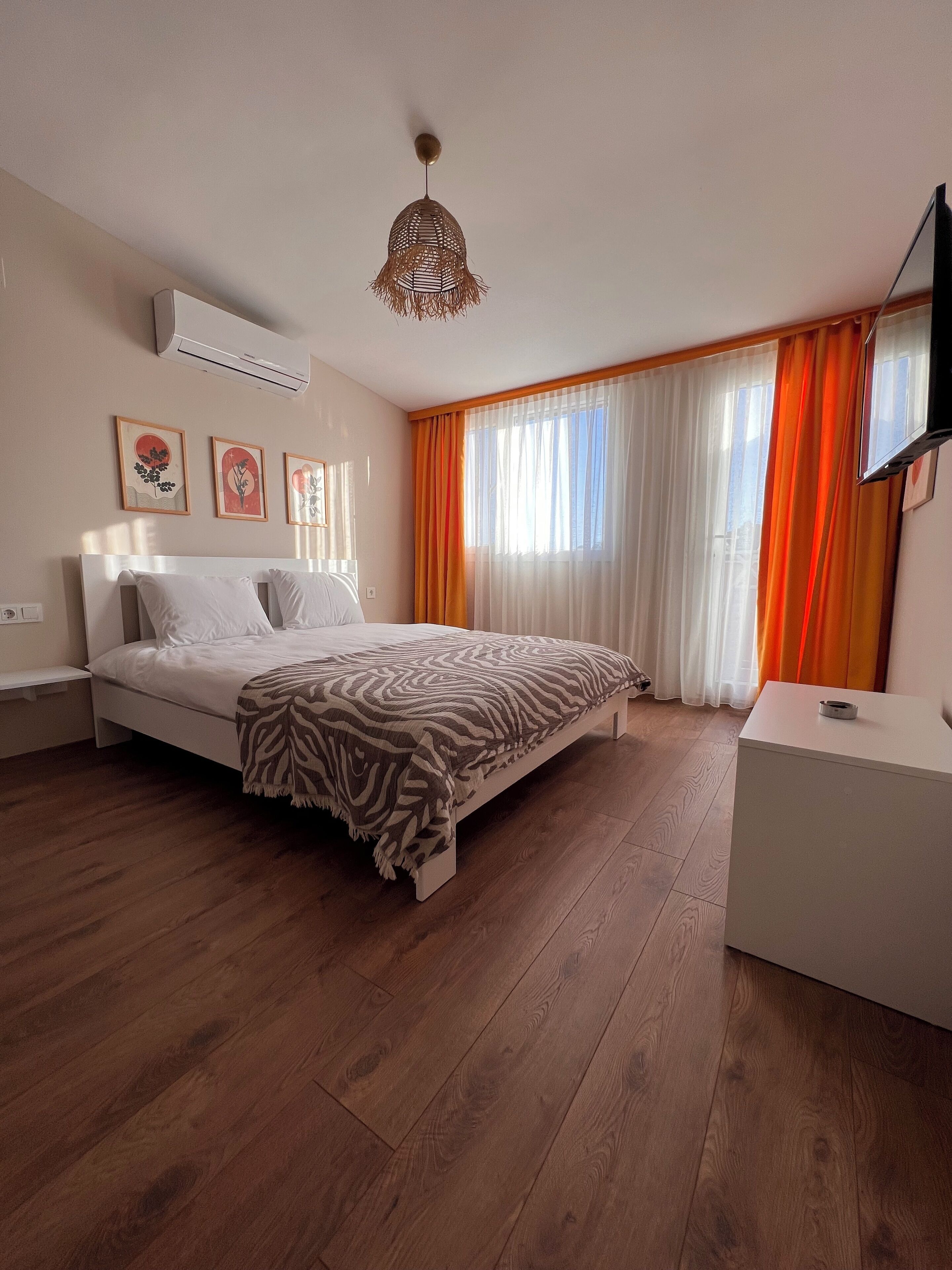 A bedroom with a bed, a bedside table, a TV, and a window with curtains.