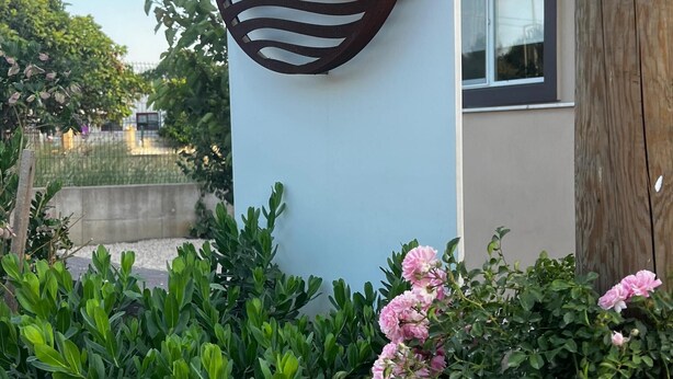 Segnaletica per 'Suite Urla', dal design moderno, immersa nel verde e circondata da fiori rosa.