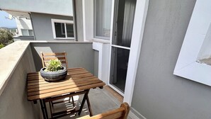 Un balcone con tavolo e sedia in legno, una pianta in vaso e una porta scorrevole in vetro.