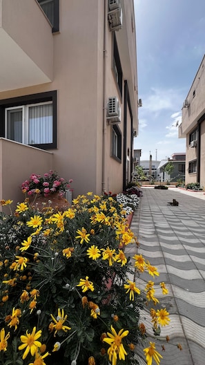 Un bâtiment doté d’une allée dallée, de climatiseurs et de parterres fleuris avec des fleurs jaunes.
