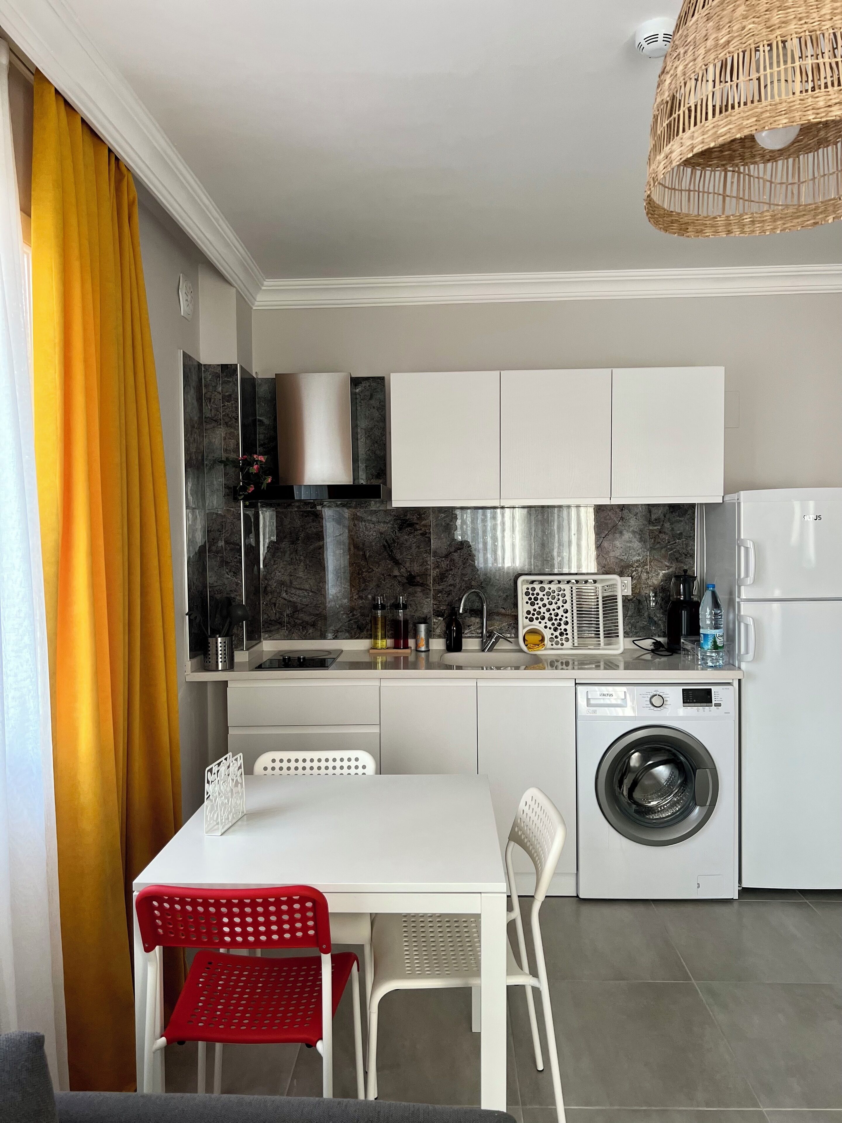 Una cocina compacta con lavadora integrada, una zona de comedor con dos sillas y una cortina amarillo brillante.