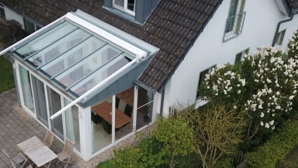 A modern house with a glass conservatory, a patio with a table and chairs, and a garden with flowering bushes. - Gästehaus Hasenkath am Deich, Gästezimmer, Bed&bike. Radwandern, Familenurlaub (Kleve)