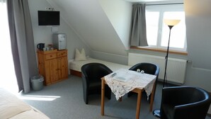 A small, cozy room with a bed, a desk with a chair, a TV, a radiator, and a window with curtains. - Gästehaus Hasenkath am Deich, Gästezimmer, Bed&bike. Radwandern, Familenurlaub (Kleve)