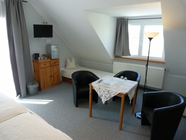 A small, cozy room with a bed, a desk with a chair, a TV, a radiator, and a window with curtains.