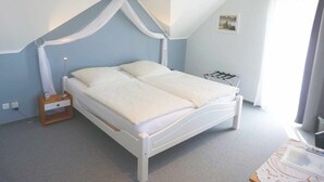A bedroom with a white bed, a nightstand with a lamp, and a window with curtains. - Gästehaus Hasenkath am Deich, Gästezimmer, Bed&bike. Radwandern, Familenurlaub (Kleve)
