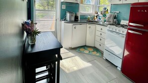 A compact kitchen with white cabinets, a red refrigerator, a gas stove, and a small window.