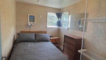 Un dormitorio con cama, cómoda, mesita de noche, estante y ventana con cortinas.