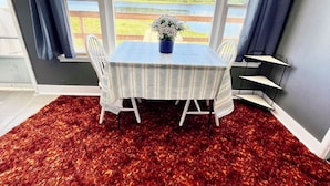 A room with a table and chairs, a window with a view of a lake and forest, and a red carpet.