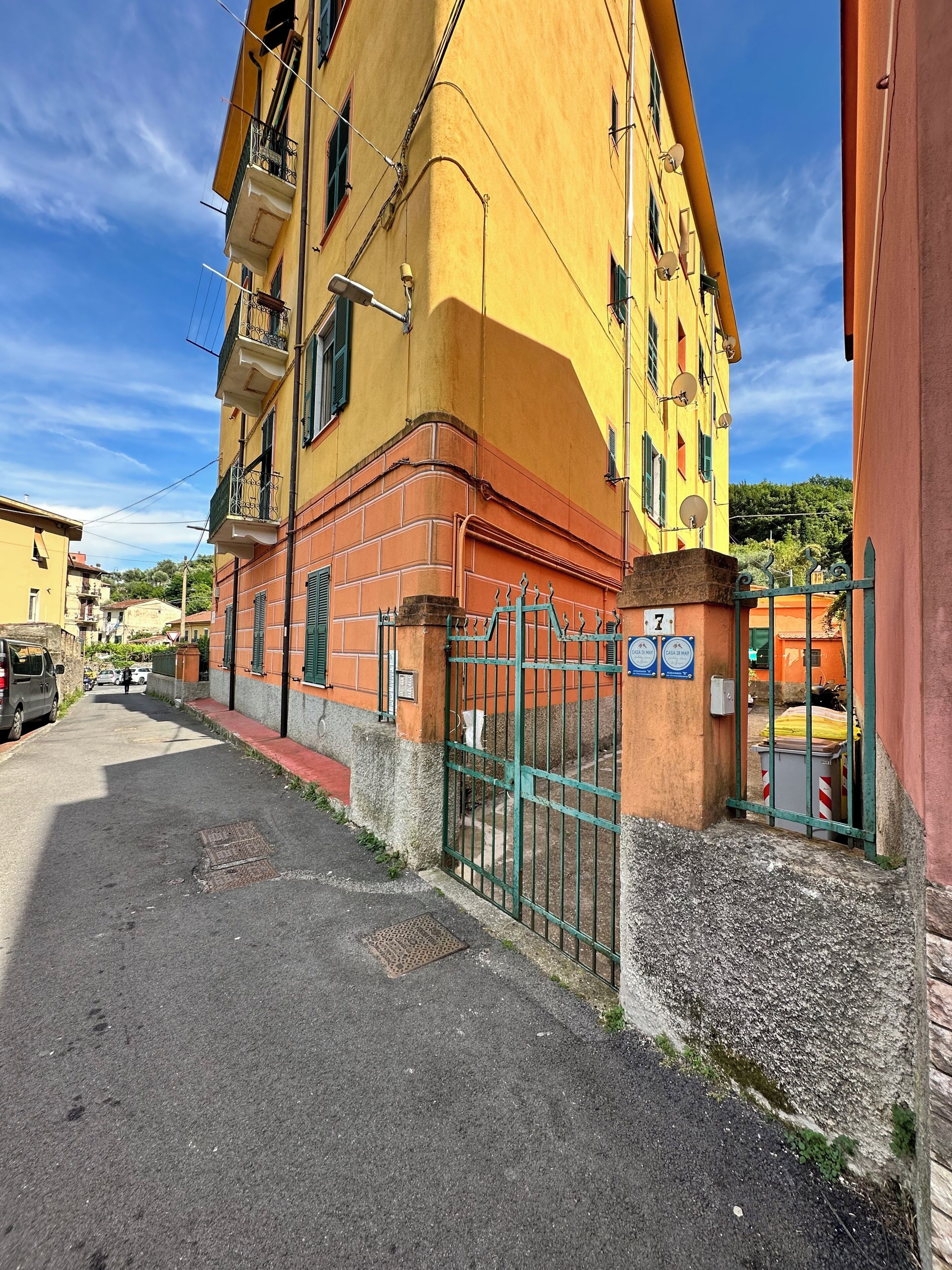 Un bâtiment jaune avec une entrée fermée par un portail, une rue bien visible et un ciel dégagé.