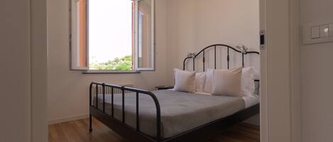 A bedroom with a metal bed frame, a window with blinds, and a radiator.