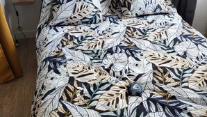 A bed with a leaf-patterned bedspread, a bedside table with a lamp, and a power outlet on the wall. - Large apartment 1st floor (Saint-Pol-de-Léon)