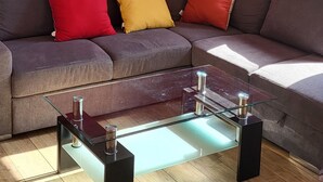 A living room with a red wall, a gray sofa with colorful cushions, a glass coffee table, and a hanging light fixture. - Large apartment 1st floor (Saint-Pol-de-Léon)