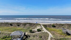 Une plage avec une structure en bois, un sentier sablonneux et l’océan en arrière-plan.