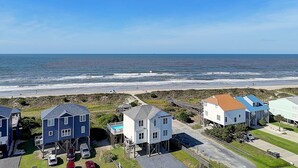 Une zone résidentielle côtière avec des maisons sur pilotis, une plage et un ciel dégagé.