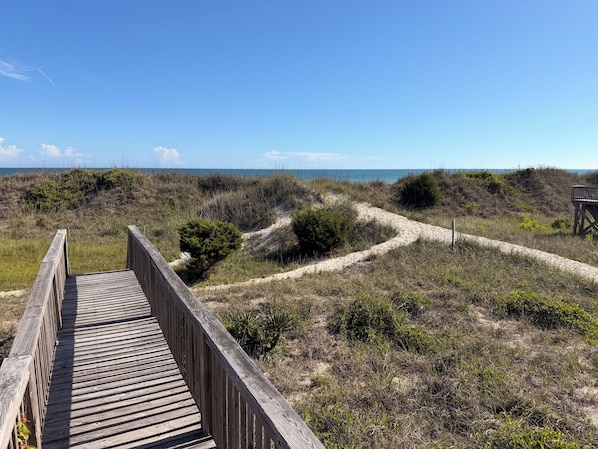 Une promenade en bois qui mène à une plage bordée de dunes et dotée d’une végétation clairsemée.
