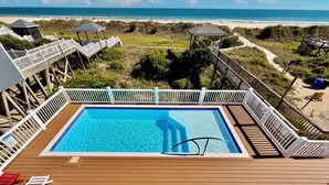 Une piscine entourée d’une terrasse en bois, de rampes blanches et de chaises de plage.
