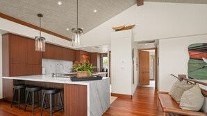 A modern kitchen with a central island, wooden bar stools, and pendant lighting.