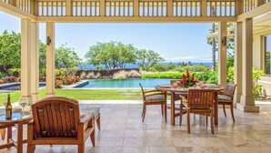 Un patio cubierto con vista a la piscina, muebles de madera y un ventilador de techo.