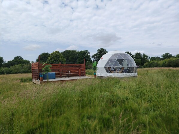 A geodesic dome structure with a wooden deck and seating area, surrounded by a grassy field and trees. - Berry Dome (Saint-Priest-la-Marche)