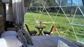 A bedroom with a large window, a bed with patterned pillows, a coffee maker, and a small table with chairs. - Berry Dome (Saint-Priest-la-Marche)