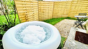 An inflatable hot tub in a backyard with a wooden fence, a stone bench, and a table with chairs.