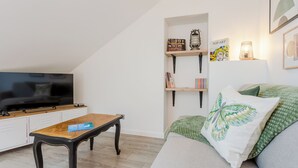 A modern living room with a flat-screen TV, a wooden coffee table, a sofa with a green cushion, and wall-mounted shelves with decorative items.