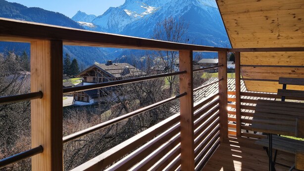Un balcón de madera con vistas a montañas nevadas y un pueblo en la falda.