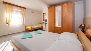 Um quarto com uma cama, um guarda-roupa de madeira, uma mesa de cabeceira com abajur, uma pequena mesa de cabeceira com abajur e uma janela com cortinas.