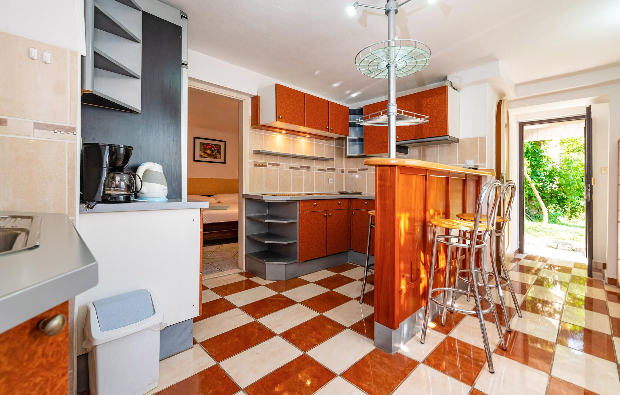 A modern kitchen with a checkered floor, wooden cabinets, a built-in stove, and a bar area with stools.