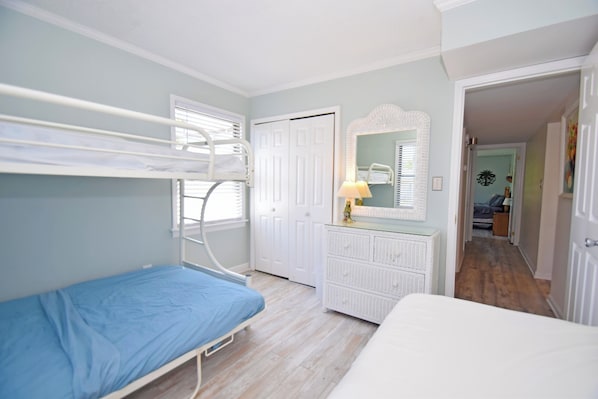 A bedroom with bunk beds, a dresser, a mirror, and a door leading to another room. - Park Place 101-Bayside 9th St, W/D, AC, Pool, WIFI (Ocean City)