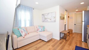Een moderne woonkamer met een beige hoekbank, een klein houten tafeltje en een keuken met een koelkast.