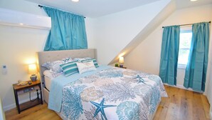 Een slaapkamer met een bed, nachtkastjes, een raam met gordijnen en een airconditioning.