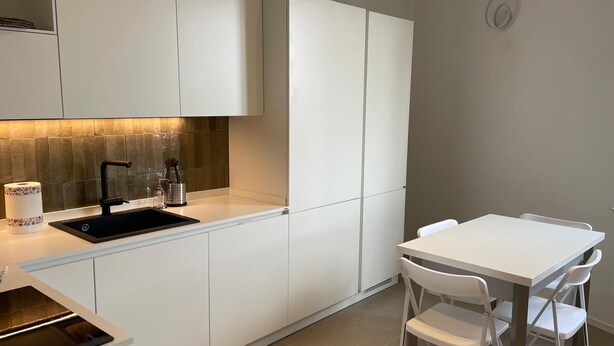 Une cuisine moderne avec des meubles blancs, un évier noir et un petit coin repas comprenant une table et des chaises blanches.