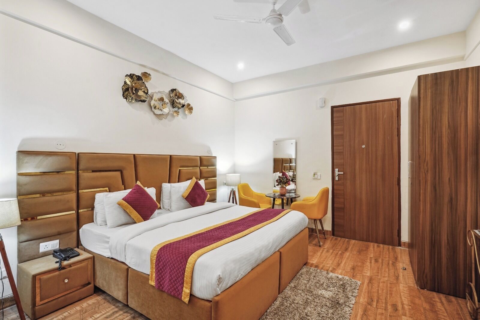 A modern hotel room with a large bed, a desk, a chair, a wardrobe, and decorative wall art.
