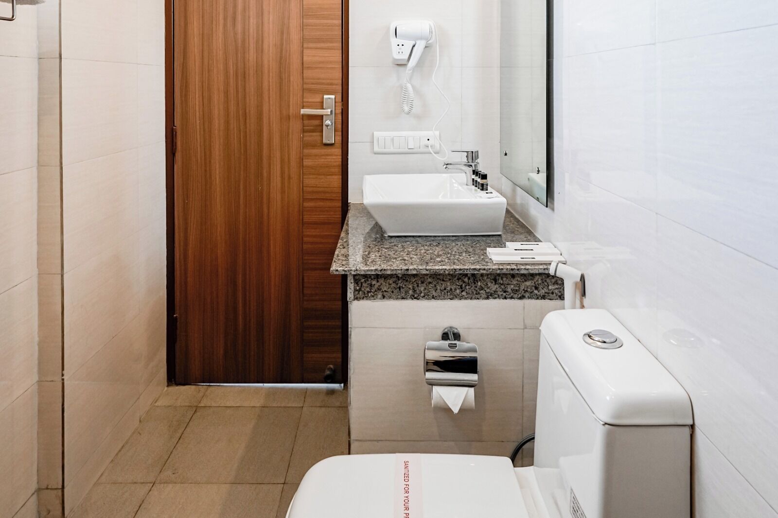 Une salle de bain moderne avec une porte en bois, un lavabo, un sèche-cheveux, des toilettes et un distributeur de serviettes.
