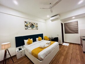 A hotel room with a bed, bedside table, lamp, ceiling fan, artwork, and a window. - Hotel Amahi Inn Near Signature Tower  (Gurugram)