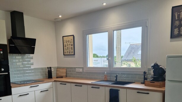 A modern kitchen with white cabinets, a wooden countertop, a built-in oven, and a window providing natural light.