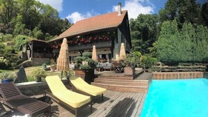 A poolside area with lounge chairs, a wooden deck, and a building with a red-tiled roof. - L'art de Vivre Avec la Nature (Fillinges)