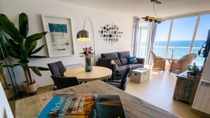 A modern living room with a dining area, featuring a large window with a view of the sea, a round table, and comfortable seating. - Front line apartment at Arenal Beach (Calpe)