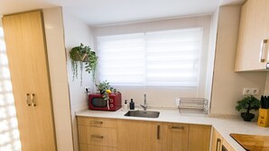 A kitchen with wooden cabinets, a microwave, a sink, and a window with blinds. - Front line apartment at Arenal Beach (Calpe)