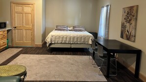 A bedroom with a bed, a desk, a chair, a door, and a painting on the wall.