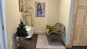 A hallway with a Christmas tree, a wicker chair with green cushions, a metal coat rack, and a framed artwork on the wall.