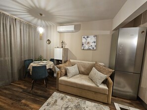 Una sala de estar con un sofá color crema, una mesa de comedor con sillas, un refrigerador y un equipo de aire acondicionado.