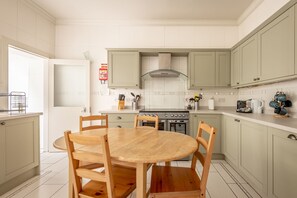 A kitchen with light green cabinets, a wooden dining table, and a stove. - House on the Burn (St Andrews)