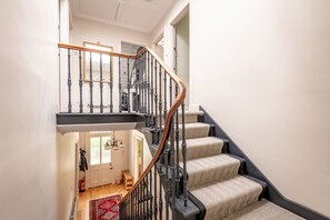 A staircase with a wooden handrail and black balusters, leading to a landing with a red patterned rug. - House on the Burn (St Andrews)